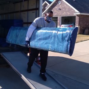 Small Move Same Day Fort Worth professional mover carefully carrying a large, shrink-wrapped furniture item down a truck ramp for a residential move in Fort Worth