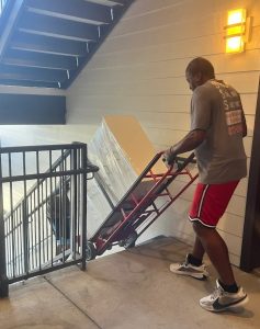 Professional appliance movers in Fort Worth carefully moving a large refrigerator down apartment stairs using a specialized dolly