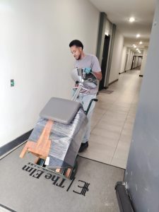 Local apartment moving specialists in Fort Worth navigating a narrow hallway with shrink-wrapped furniture