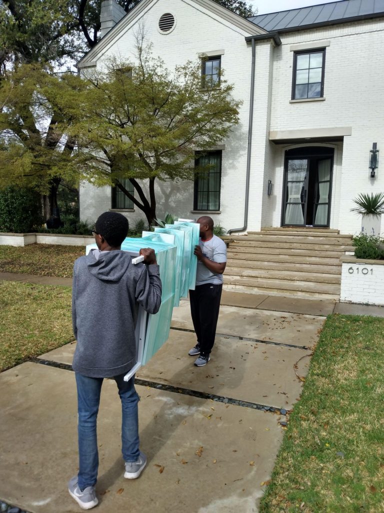 Professional local residential home movers in Fort Worth carefully carrying a large piece of furniture into a white brick house.