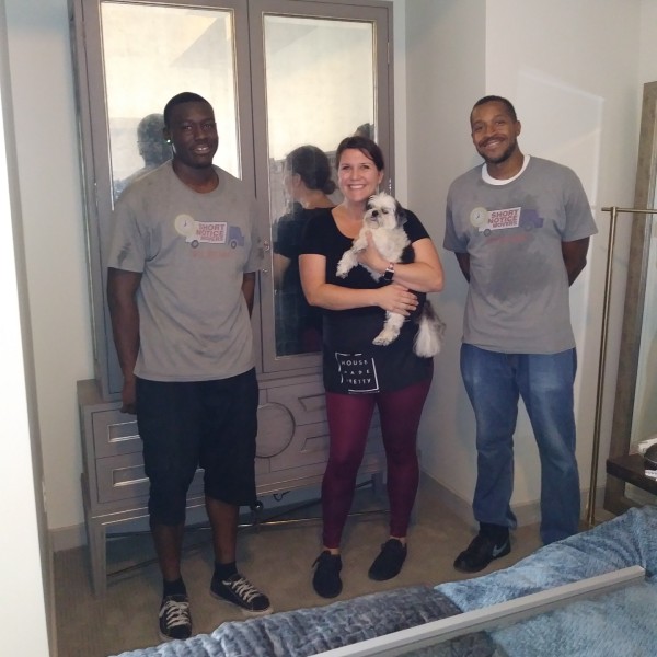 Professional movers in Fort Worth standing with a happy customer and her dog after completing furniture packing and protection.