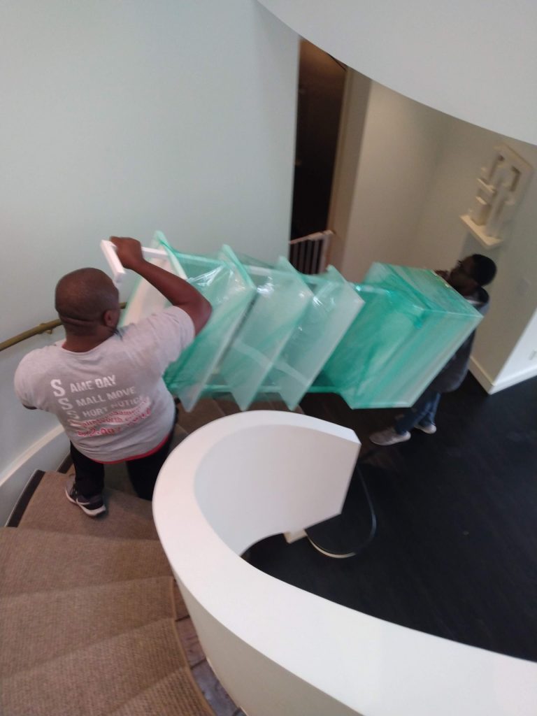 Two professional movers in Fort Worth providing white glove moving services for protected furniture down a residential staircase.
