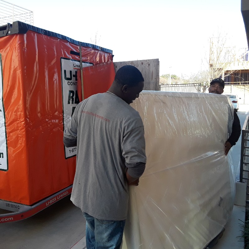 Professional movers in Fort Worth providing same-day labor help to load a U-Haul U-Box container with shrink-wrapped furniture