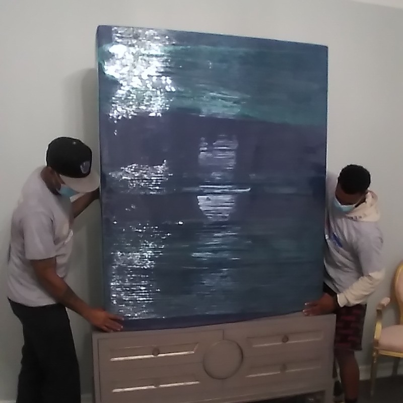 Professional movers in Fort Worth carefully placing a large, shrink-wrapped piece of furniture onto a dresser during a residential move.